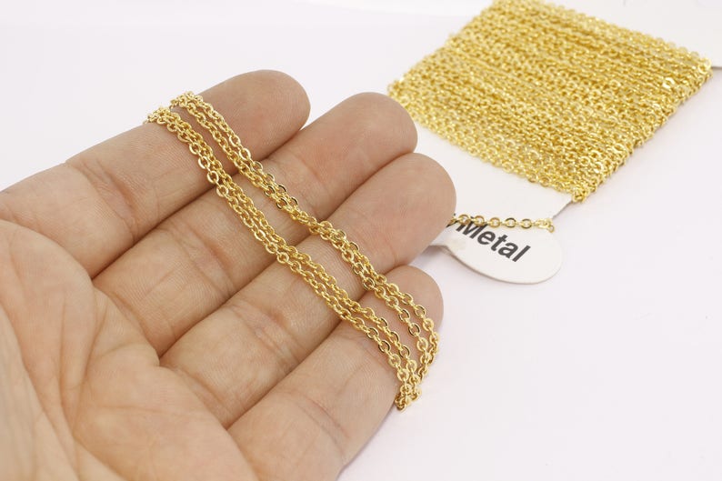 Puede incluir: Collar de cadena de color dorado con un dise&ntilde;o delicado de doble hebra. La cadena se sostiene en una mano, con un carrete de cadena adicional visible en el fondo. La etiqueta dice "Metal".