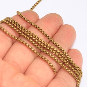 Op de afbeelding: Close-up van verschillende strengen goudkleurige ketting. De ketting is gemaakt van kleine, ronde schakels, waardoor een textuur ontstaat. De kettingen worden in een hand tegen een witte achtergrond gehouden.