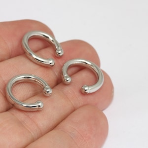 May include: Three silver-colored, curved ear cuffs. Each cuff has a rounded ball at each end. The ear cuffs are displayed on a light background.