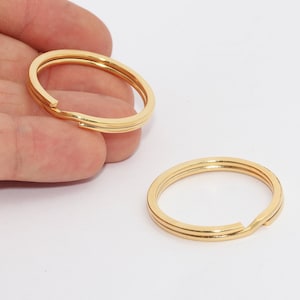 Può includere: Due portachiavi color oro. Ogni anello è di forma ovale con un'apertura per aggiungere chiavi. Gli anelli hanno una finitura metallica lucida. Un anello è tenuto in mano, mentre l'altro è su una superficie bianca.