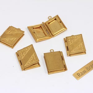 Könnte beinhalten: Mehrere kleine, goldfarbene Messingmedaillons und ein kleines rechteckiges Messingschild mit der Aufschrift "Raw Brass" sind auf einer weißen Oberfläche angeordnet. Die Medaillons sind in verschiedenen Zuständen geöffnet und geschlossen.