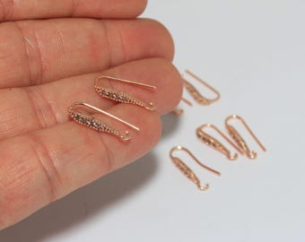 May include: A collection of rose gold-toned earring hooks featuring a slender, elongated design with a textured surface. Each hook includes a small loop at the bottom for attaching charms or pendants, and the metal has a polished, metallic finish.