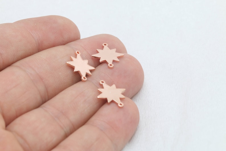 May include: Three rose gold star charms with eight points, each featuring a small loop at the top and bottom for stringing. The charms are displayed against a neutral background, ideal for jewelry making or crafting.