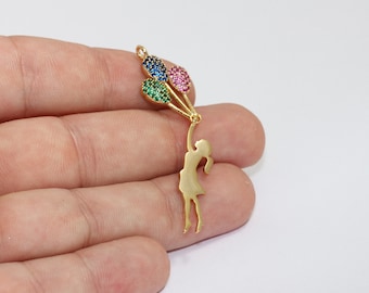 May include: A gold-colored charm featuring a silhouette of a person holding three colorful gem-studded balloons. The balloons are in blue, green, and pink. The charm is designed to be a pendant or a decorative element.