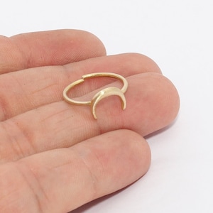 May include: A gold-colored ring featuring a crescent moon design. The ring is delicate and appears to be adjustable. The moon is the focal point, adding a celestial touch to the jewelry. The ring is shown against a white background.