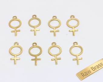 May include: Eight gold-colored brass charms in the shape of the female symbol, each with a small loop at the top for attaching to jewelry. A small brass rectangle with the text "Raw Brass" is also included.