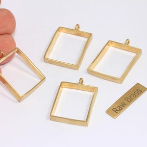 Könnte beinhalten: Vier goldfarbene rechteckige Anhängerrahmen aus Messing mit einer kleinen Schlaufe oben zum Aufhängen. Ein kleines Messingschild mit dem Text "Raw Brass" ist ebenfalls vorhanden. Die Rahmen sind leer.