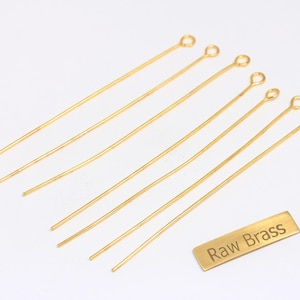 Puede incluir: Un conjunto de alfileres de ojo dorados, ideales para la fabricación de joyas. Los alfileres son rectos con un extremo en bucle. También hay una pequeña etiqueta rectangular con las palabras "Raw Brass".