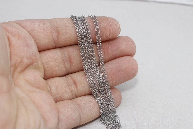 Puede incluir: Una colecci&oacute;n de collares de cadena de color plateado. Las cadenas son finas y delicadas, con un acabado met&aacute;lico brillante. Las cadenas se sostienen en una mano sobre un fondo blanco.