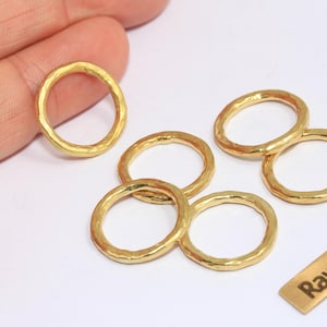 Peut inclure: Plusieurs anneaux en laiton doré martelé sont présentés sur une surface blanche. Une petite étiquette rectangulaire porte l'inscription "Raw Brass". Les anneaux ont une surface texturée et une forme circulaire.