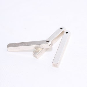 May include: Three silver metal bars with a rectangular shape and rounded edges are arranged on a white background. Each bar has a small, dark hole at one end. The bars appear to be components of a larger item.