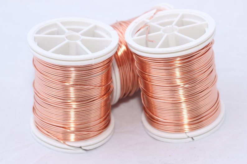 May include: Three spools of copper wire are displayed against a white background. The wire is tightly wound around white plastic spools. The copper wire has a shiny, reddish-brown color, and the spools are evenly spaced.