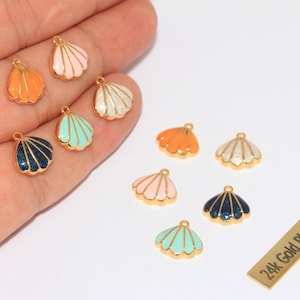 Könnte beinhalten: Eine Sammlung bunter Muschelanhänger in Orange, Rosa, Weiß, Türkis und Marineblau mit goldfarbenem Rand. Die Anhänger sind klein und haben oben eine Schlaufe zum Befestigen an Schmuck. Ein kleines goldfarbenes Rechteck trägt die Aufschrift "24k Gold Plated".