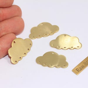 Könnte beinhalten: Vier Messing-Wolkenanhänger mit gewellten Kanten und vorgebohrten Löchern für die Schmuckherstellung. Ein kleines Messingrechteck mit dem Text "Raw Brass" ist ebenfalls vorhanden. Ideal für die Herstellung von Ohrringen, Halsketten oder anderen Bastelprojekten.