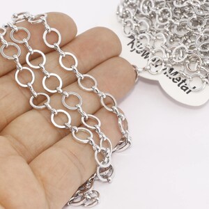 May include: Close-up of a silver-colored chain with a series of interconnected open circles. The chain is held in a hand against a white background. The chain is labeled with the text "KJW Metal".