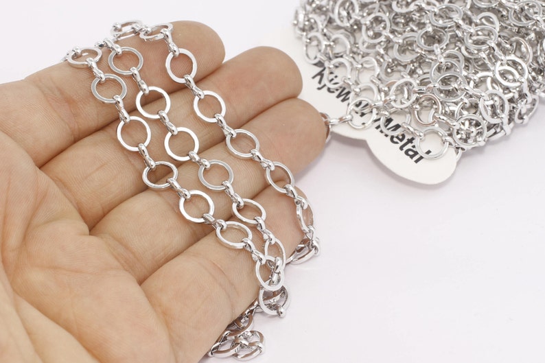 May include: Close-up of a silver-colored chain with a series of interconnected open circles. The chain is held in a hand against a white background. The chain is labeled with the text "KJW Metal".