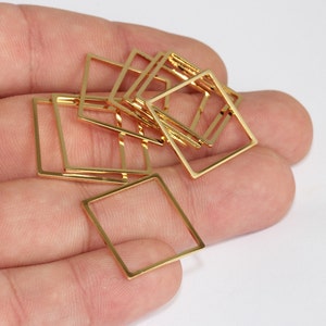Op de afbeelding: Een verzameling kleine, goudkleurige vierkante metalen frames. De frames zijn in het midden open en lijken van dun metaal te zijn gemaakt. Ze zijn verspreid op een lichte achtergrond.