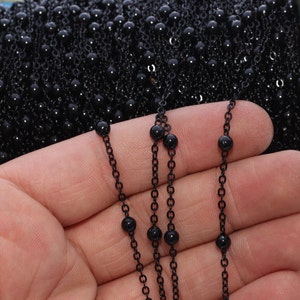 May include: Black beaded chain on a spool. The chain features small, round black beads spaced along a delicate black chain. The beads are approximately 3mm in diameter. The chain is shown against a white background.