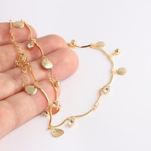 May include: Gold-coloured anklet with heart and shell charms, and clear crystal details. The delicate chain has an adjustable length. The anklet design combines straight and curved lines.