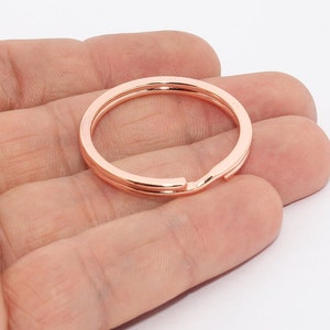 Può includere: Un portachiavi diviso in metallo oro rosa. L'anello portachiavi è rotondo con un design a doppio anello. Il portachiavi è tenuto in mano da una persona su sfondo bianco. Il portachiavi ha un diametro di circa 3,2 cm.