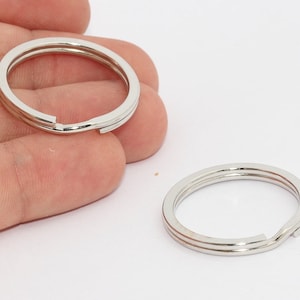 Può includere: Due portachiavi divisi color argento. Ogni anello è circolare con una fessura per aggiungere chiavi. Gli anelli hanno una finitura metallica lucida e sono mostrati su sfondo bianco. Gli anelli sono progettati per contenere chiavi o altri piccoli oggetti.