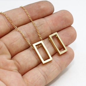 May include: A gold-coloured necklace with a rectangular pendant and a matching rectangular earring. The necklace has a delicate chain. The jewellery is displayed against a light background.