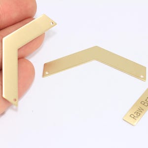 May include: Three raw brass jewelry components. Two are chevron-shaped with holes for attaching to other pieces. A small rectangular piece is engraved with the words "Raw Brass". The components are a warm gold color.