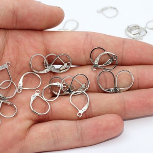May include: A selection of silver-coloured leverback earring findings, presented against a light backdrop. The findings are arranged in different orientations, highlighting their design. These findings are used in jewellery making.