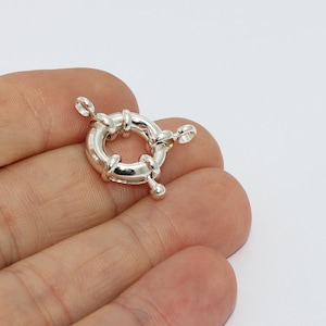 May include: A shiny, silver-colored spring ring clasp. The clasp is circular with a central ring and a hinged opening mechanism. It has small loops for attaching to jewelry pieces. The clasp is designed for secure closure and is suitable for various jewelry applications.