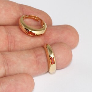 May include: Two gold-colored rings with a rectangular orange gemstone. One ring is on a finger, and the other is lying flat. The rings have a smooth, polished finish and a simple, elegant design. Jewelry.
