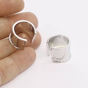 May include: Two silver-colored ear cuffs. The ear cuffs have a simple, modern design with a smooth, reflective surface. The cuffs are open at one end, designed to wrap around the ear. The jewelry is displayed against a white background.