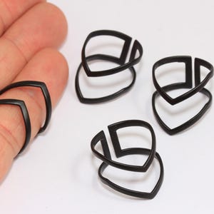 Op de afbeelding: Zwarte gitaarvingerplectrums. De plectrums zijn gemaakt van een donker materiaal en hebben een uniek ontwerp. Eén zit op een vinger en drie liggen op een wit oppervlak. Deze plectrums zijn ontworpen om op de vingers te worden gedragen tijdens het gitaarspelen.