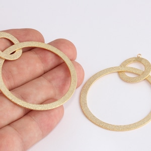 Puede incluir: Dos componentes de pendientes de metal texturizado de color dorado. Cada componente presenta un gran bucle circular conectado a un bucle ovalado más pequeño. Los pendientes tienen una superficie texturizada y un pequeño bucle en la parte superior para la fijación.