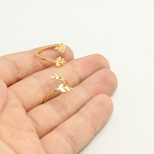 May include: Two gold-colored, open-ended rings with leaf designs. The rings are displayed on a light background. The rings are open, allowing for an adjustable fit. The leaf design adds a touch of nature-inspired elegance to the jewelry.