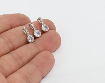 May include: Three silver pendants with a clear, round gemstone and a small loop adorned with small, clear stones. The pendants are displayed against a white background.