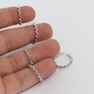 May include: Several silver rings with a chain-link design are displayed against a white background. One ring is open, adjustable, and the others are closed. The rings are small and delicate, suitable for stacking or wearing individually.