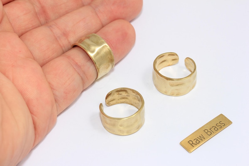 May include: Close-up of three raw brass rings with a hammered texture. One ring is on a finger, and two are open-ended. A small brass rectangle with the text "Raw Brass" is also present.