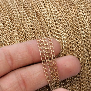 Puede incluir: Primer plano de un carrete de cadena dorada. Varios hilos de la cadena se sostienen en una mano, mostrando los pequeños eslabones ovalados. La cadena probablemente se utiliza para la fabricación de joyas u otras manualidades.