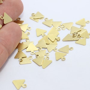 May include: A selection of small, gold-coloured triangle charms with a loop at the top, ideal for jewellery making. The charms are scattered on a white surface, with some held in a hand. The triangles are flat and have a matte finish.