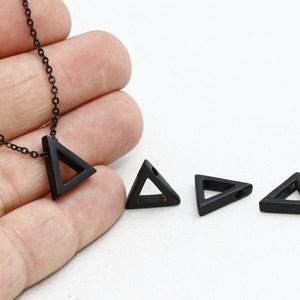 Könnte beinhalten: Eine schwarze geometrische Halskette mit einem dreieckigen Anhänger an einer feinen Kette. Drei zusätzliche schwarze Dreiecksanhänger sind abgebildet. Der Schmuck ist vor einem weißen Hintergrund platziert, was das minimalistische Design hervorhebt.