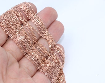 May include: Close-up of multiple strands of delicate, rose gold-colored chain. The chains are made of small, evenly spaced links, creating a shimmering effect. The chains are held in a hand against a white background. Ideal for jewelry making.