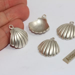 May include: Four antique silver seashell charms with a textured finish. Each charm has a loop for attaching to jewellery. A small rectangular tag with the words "Antique Silver" is also present.