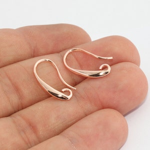 Puede incluir: Dos ganchos para pendientes de oro rosa. Los ganchos tienen forma de lágrima con un diseño curvo. Los ganchos están hechos de un metal brillante. Los ganchos se muestran sobre un fondo claro.