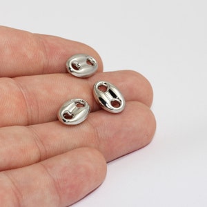 May include: Three shiny, silver-colored, oval-shaped jewelry findings. Each finding has two holes for attaching to other jewelry components. The findings are smooth and reflective, with a polished finish. They are displayed on a white background.