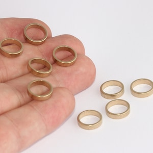 May include: A collection of small, gold-colored metal rings. The rings are circular with a flat profile and are scattered across a white background. The rings are likely jewelry components or craft supplies.