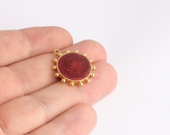 May include: A gold-colored pendant with a circular, maroon-colored center. The pendant has a textured, swirling pattern within the maroon circle. Small, gold-colored beads surround the maroon center. A small loop is at the top for attaching to a chain or other jewelry.