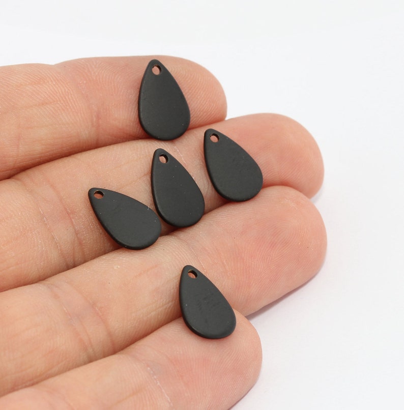 May include: A collection of six matte black teardrop-shaped charms. Each charm has a small hole at the top for stringing. The charms are displayed against a white background.