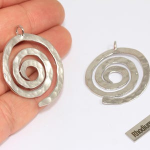 May include: Two silver-coloured spiral pendants with a hammered texture. The pendants have a loop at the top for hanging. A small rectangular tag with the text "Rhodium Plated" is also visible.