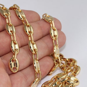 May include: A gold-colored chain necklace with a coffee bean link design. The links are oval-shaped with a central bar, creating a unique and eye-catching pattern. The chain is displayed against a white background.