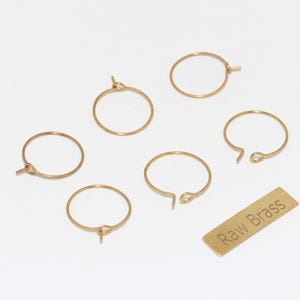 May include: A collection of gold-colored brass earring hoops and a small rectangular brass tag with the text "Raw Brass". The hoops vary in design, some with clasps and others open.
